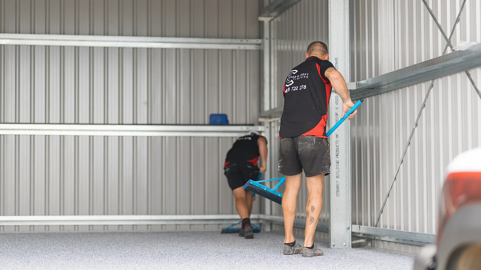 Two installers spreading decorative flakes across a new epoxy shed floor