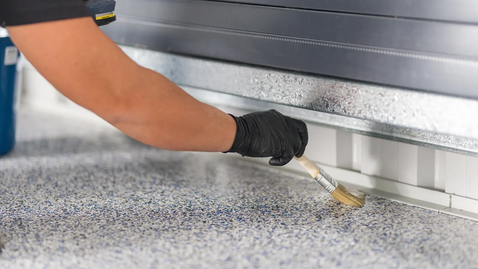Close-up of a gloved hand brushing clear epoxy onto a flake floor edge