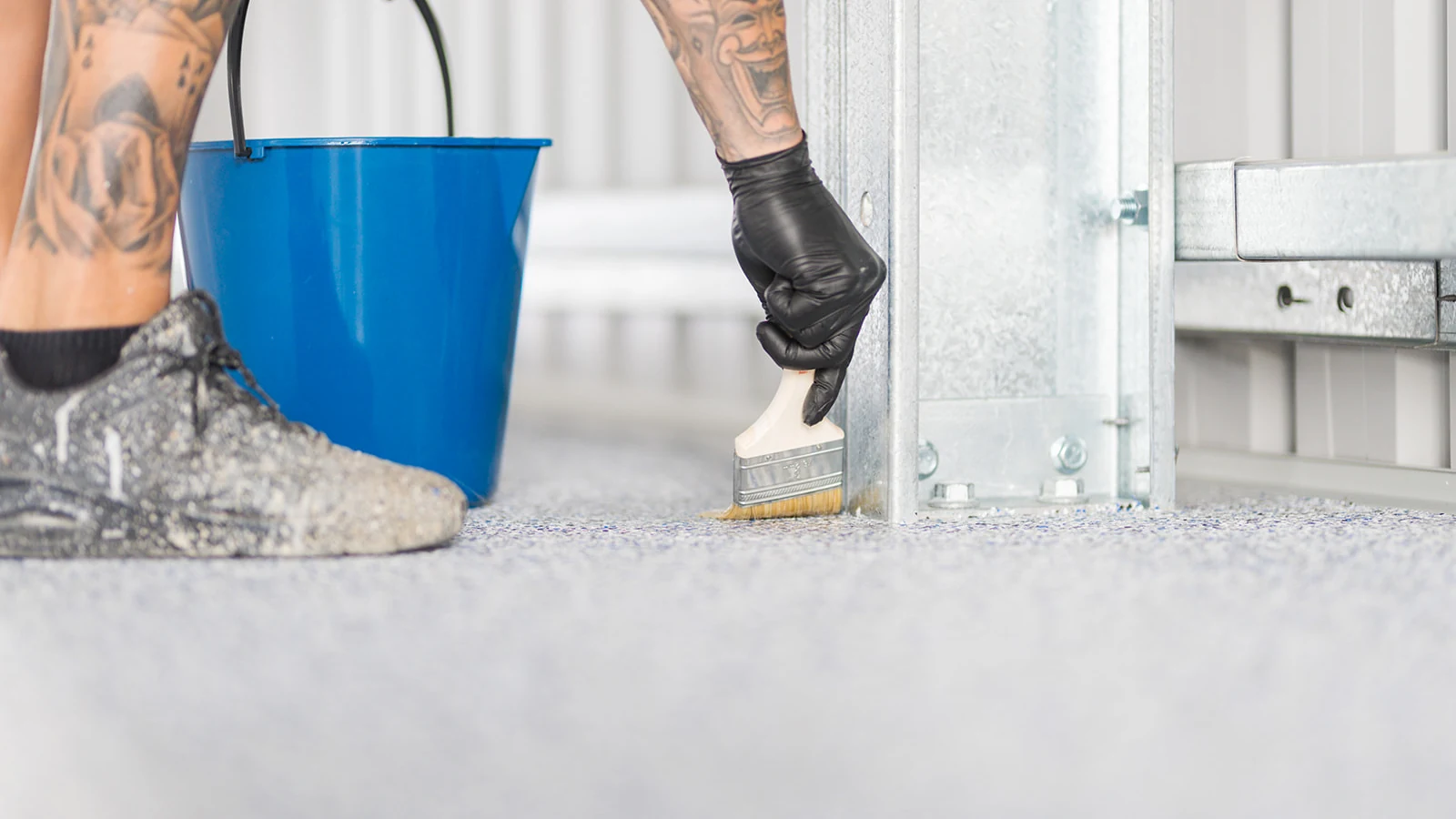 Gloved installer brushing clear sealer around a steel shed post