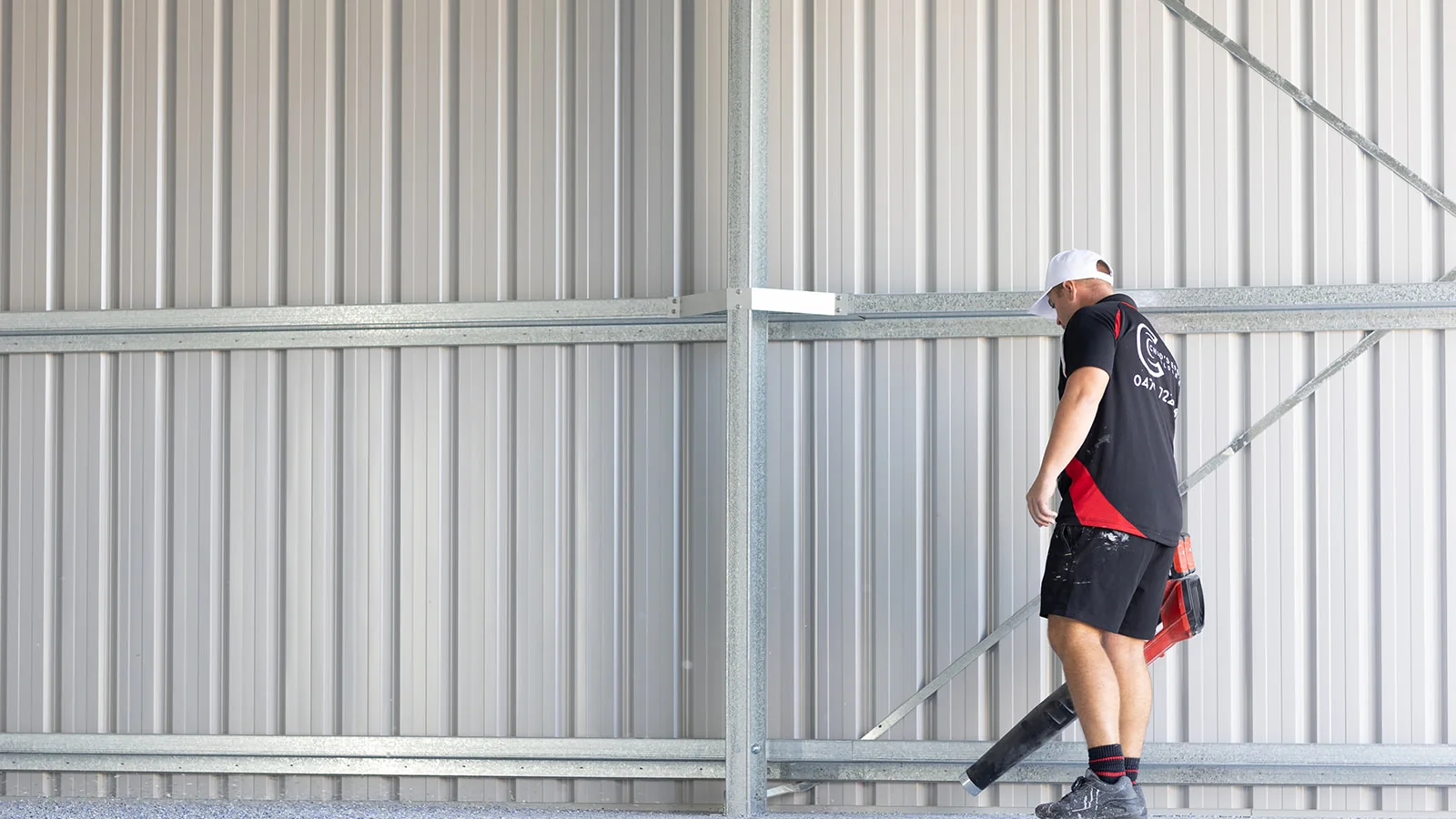 Epoxy technician clearing loose flakes with a blower inside a steel shed