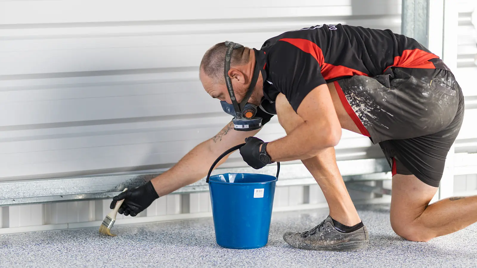 Installer wearing a respirator brushing sealer onto flake floor edges