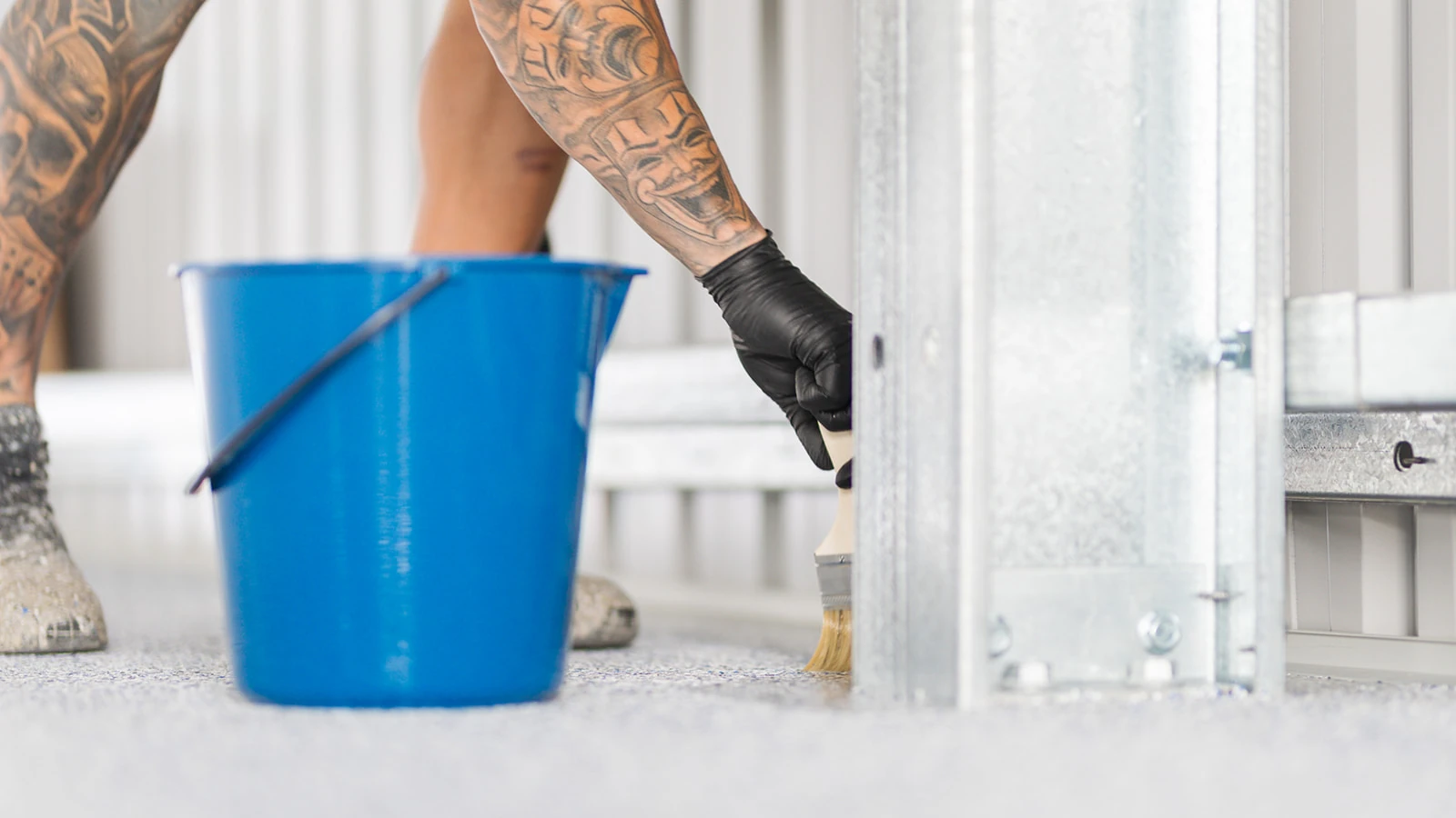 Blue epoxy bucket beside an installer brushing sealer near a shed post