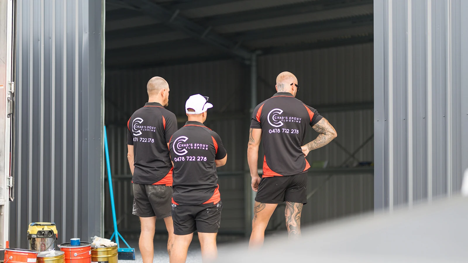 Three epoxy flooring installers planning a shed floor coating with EpiMax epoxy tins ready