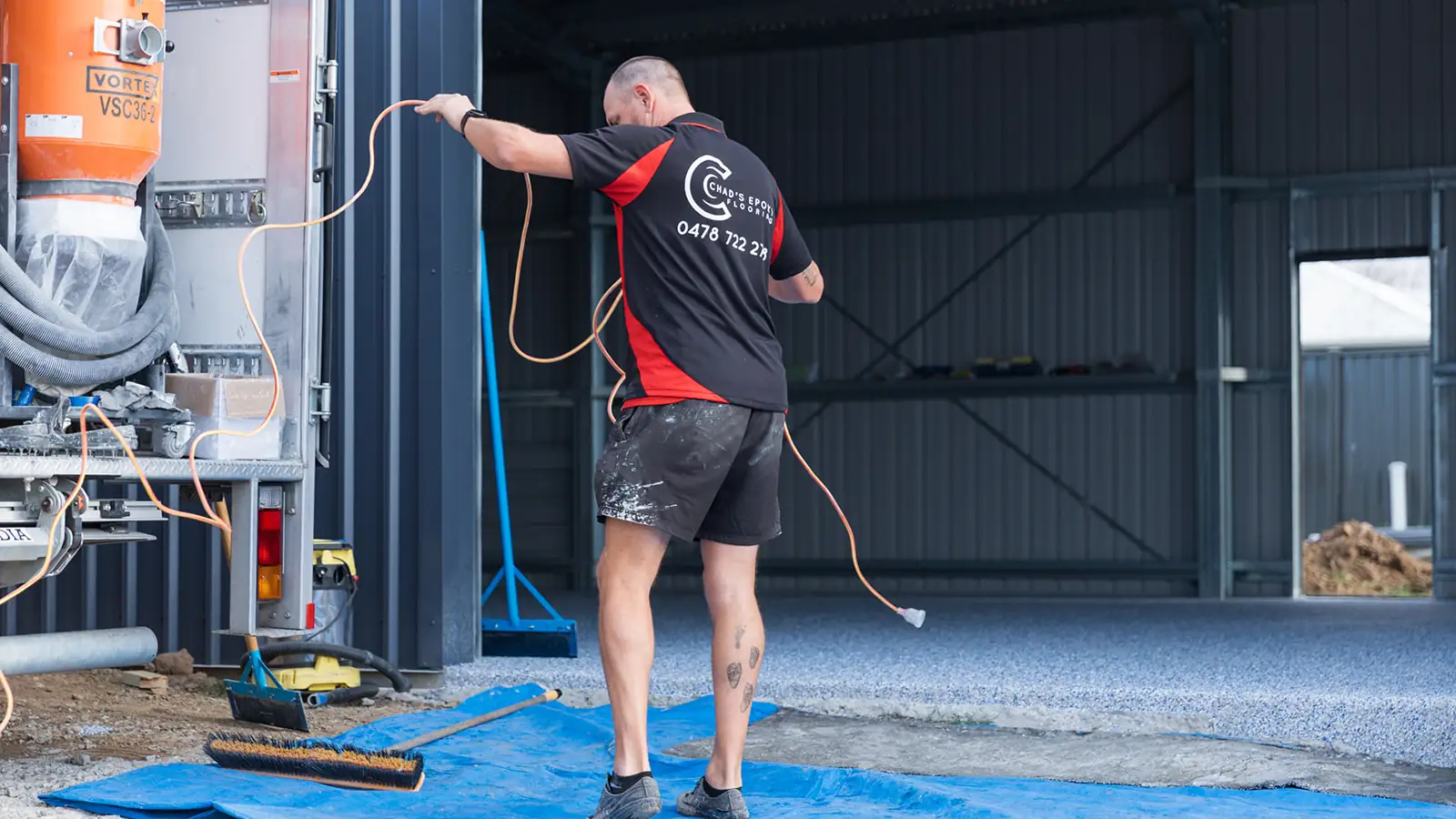 Installer setting up power leads for floor grinding equipment at a shed epoxy job