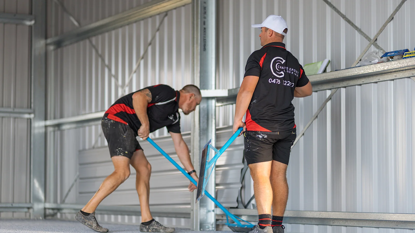 Two epoxy installers scraping excess flakes from a shed floor coating