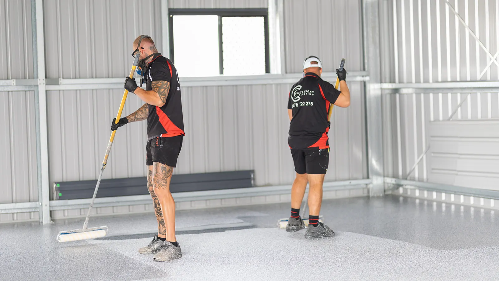 Epoxy team applying clear topcoat to a grey flake floor in a Marburg shed