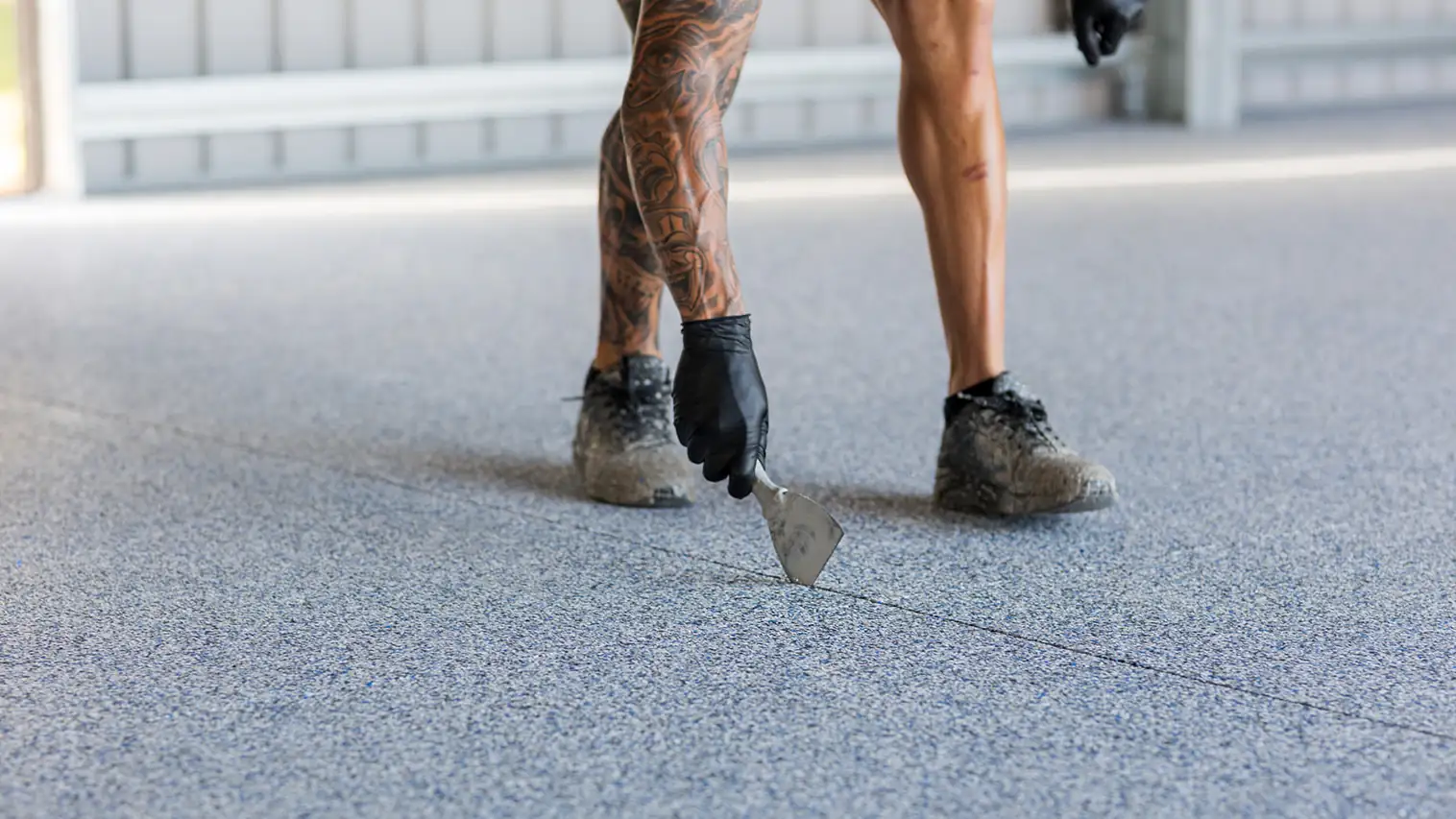 Gloved installer scraping the edge of a grey flake epoxy floor