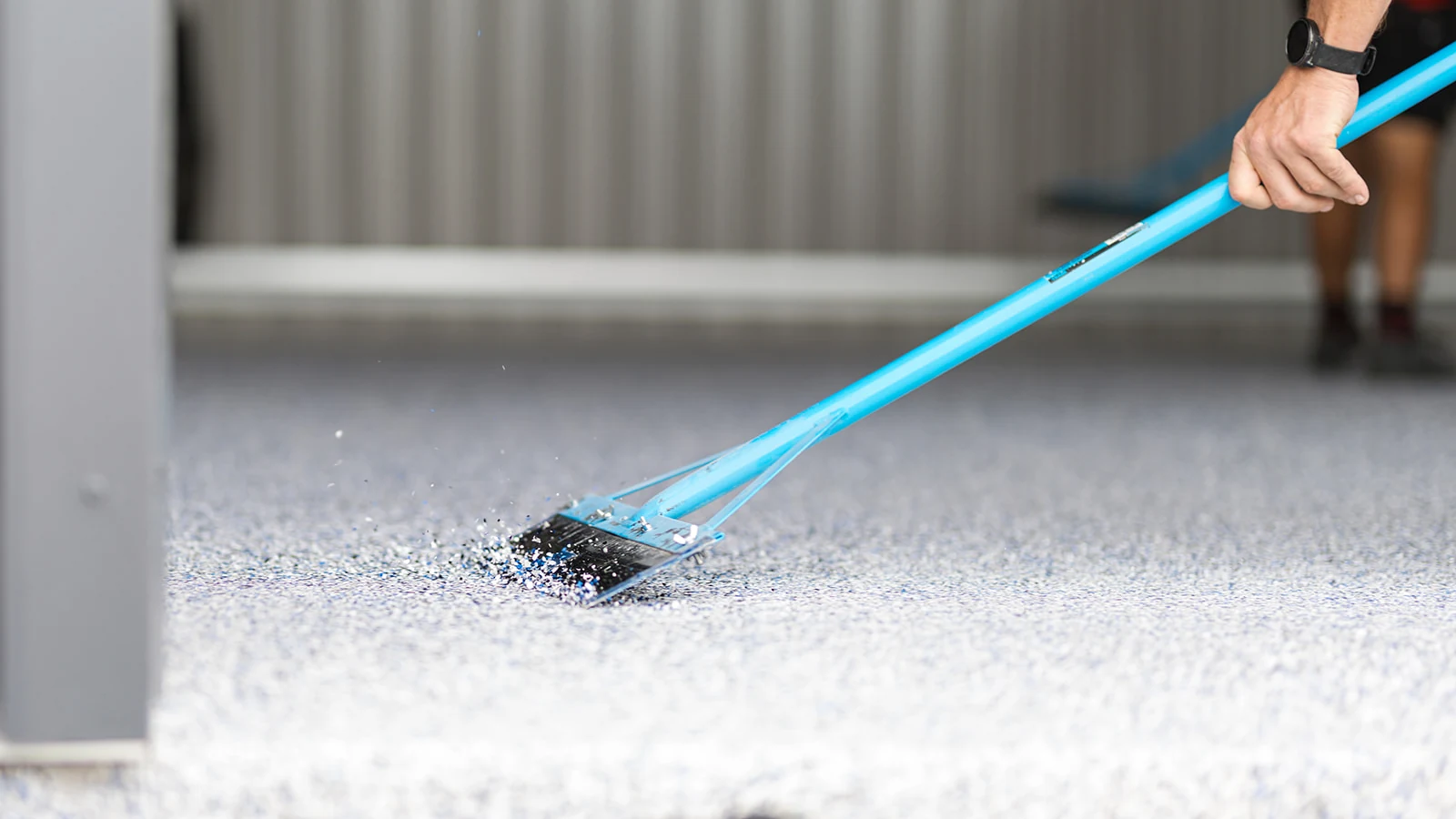 Close-up of a scraper tool levelling decorative epoxy flakes on a shed floor