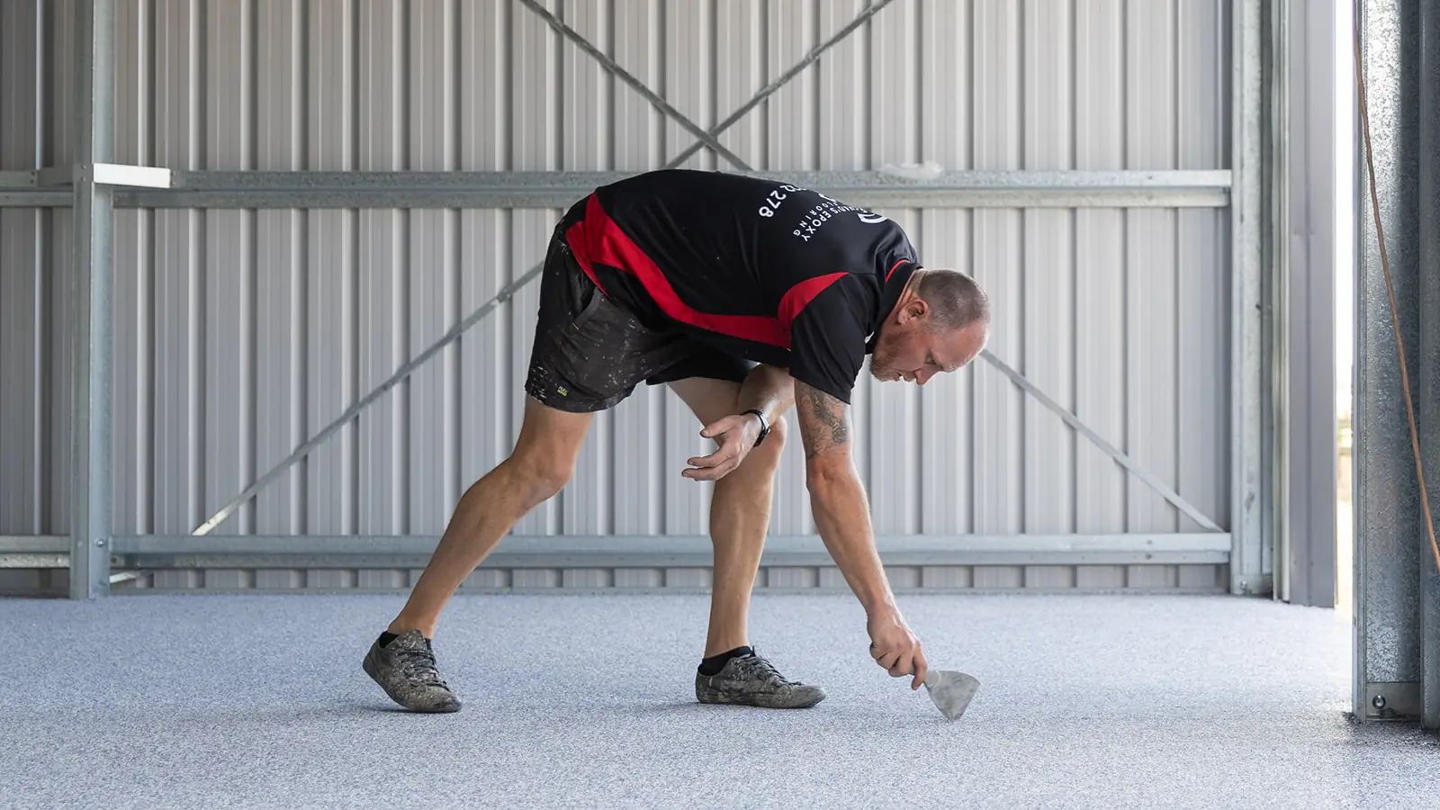 Epoxy installer hand scraping rough spots on a grey flake shed floor