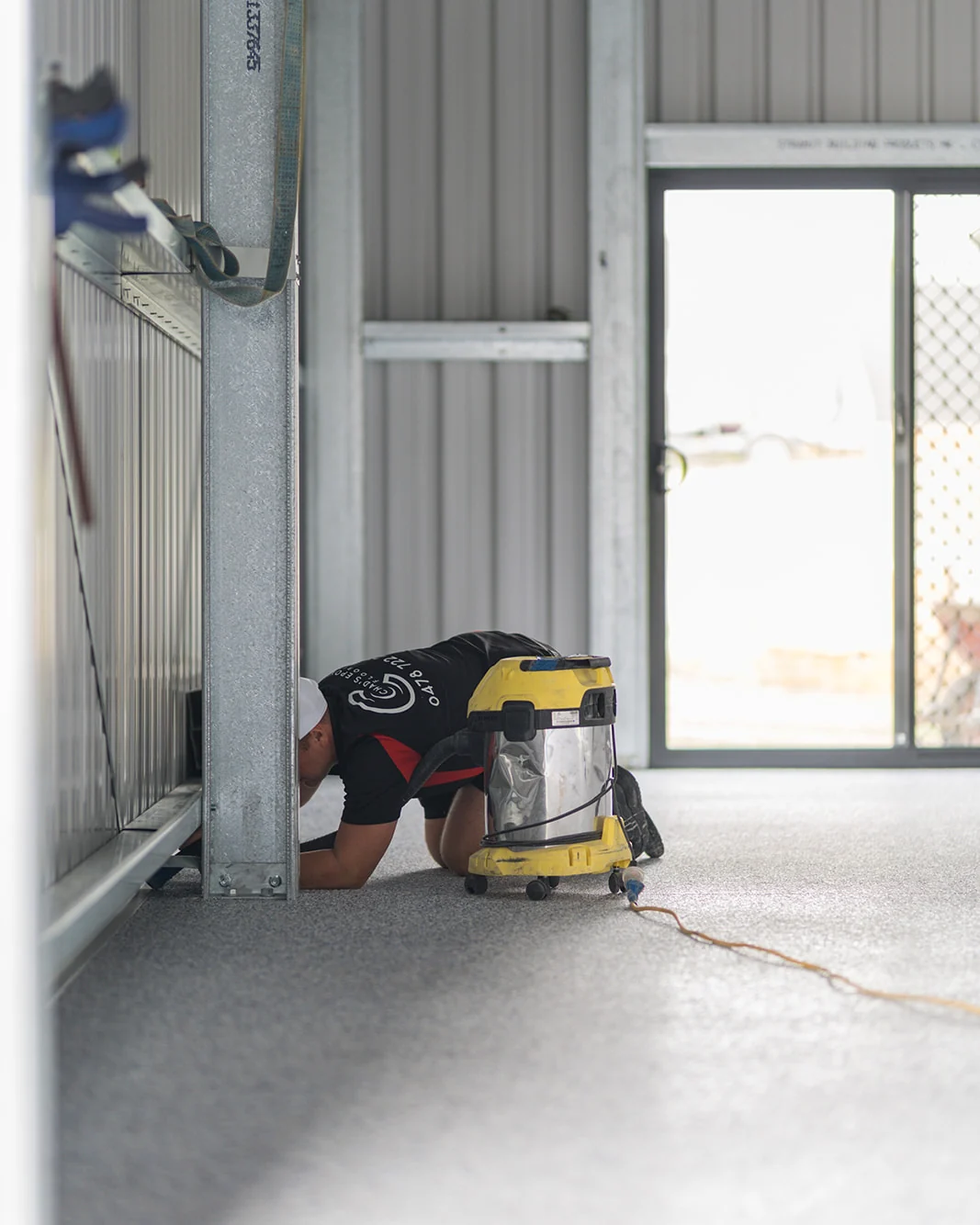 Installer vacuuming a flake epoxy floor with an industrial vacuum inside a shed
