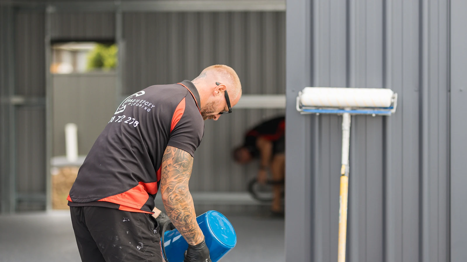 Epoxy installer mixing clear topcoat in a bucket beside a roller