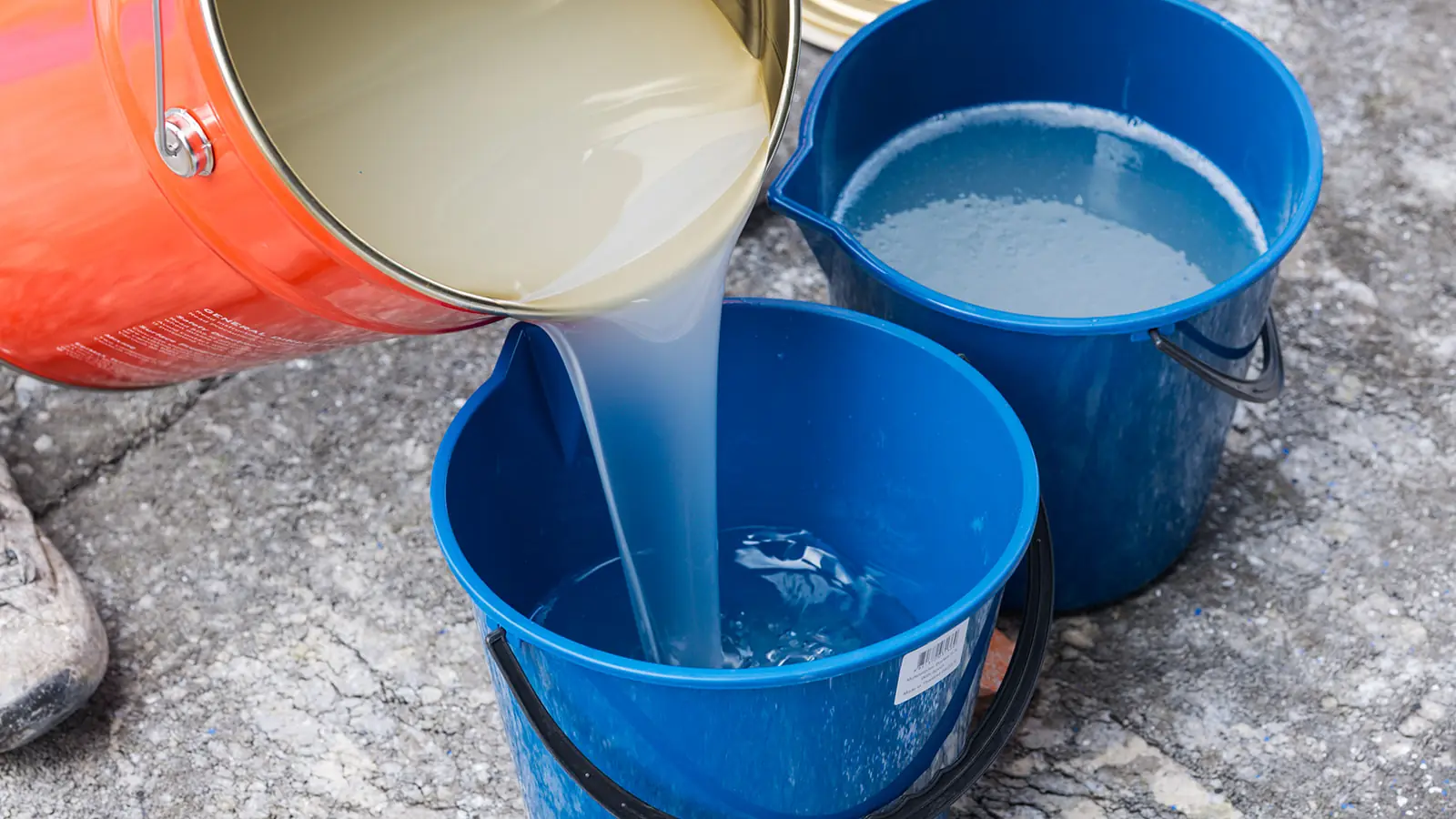 Clear epoxy being poured from an EpiMax tin into blue mixing buckets