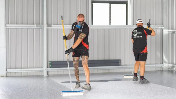 Two Chad's Epoxy installers rolling clear topcoat onto a flake shed floor