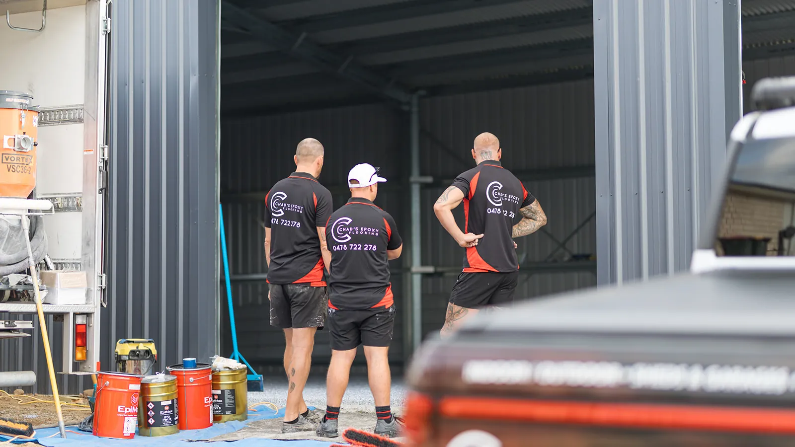 Epoxy crew preparing a shed floor job with the equipment truck and coating tins set up