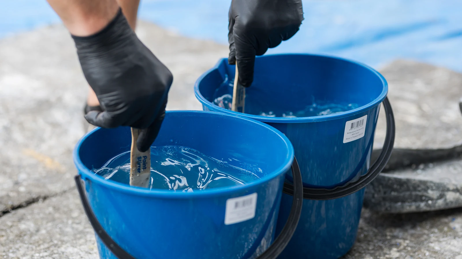 Gloved hands stirring clear epoxy in blue mixing buckets
