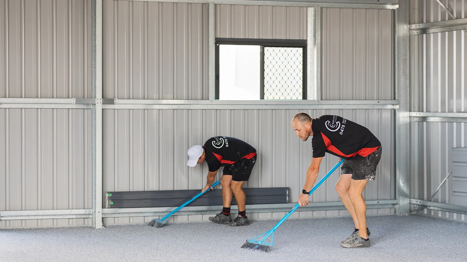 Two Chad's Epoxy installers scraping excess flakes across a new shed floor